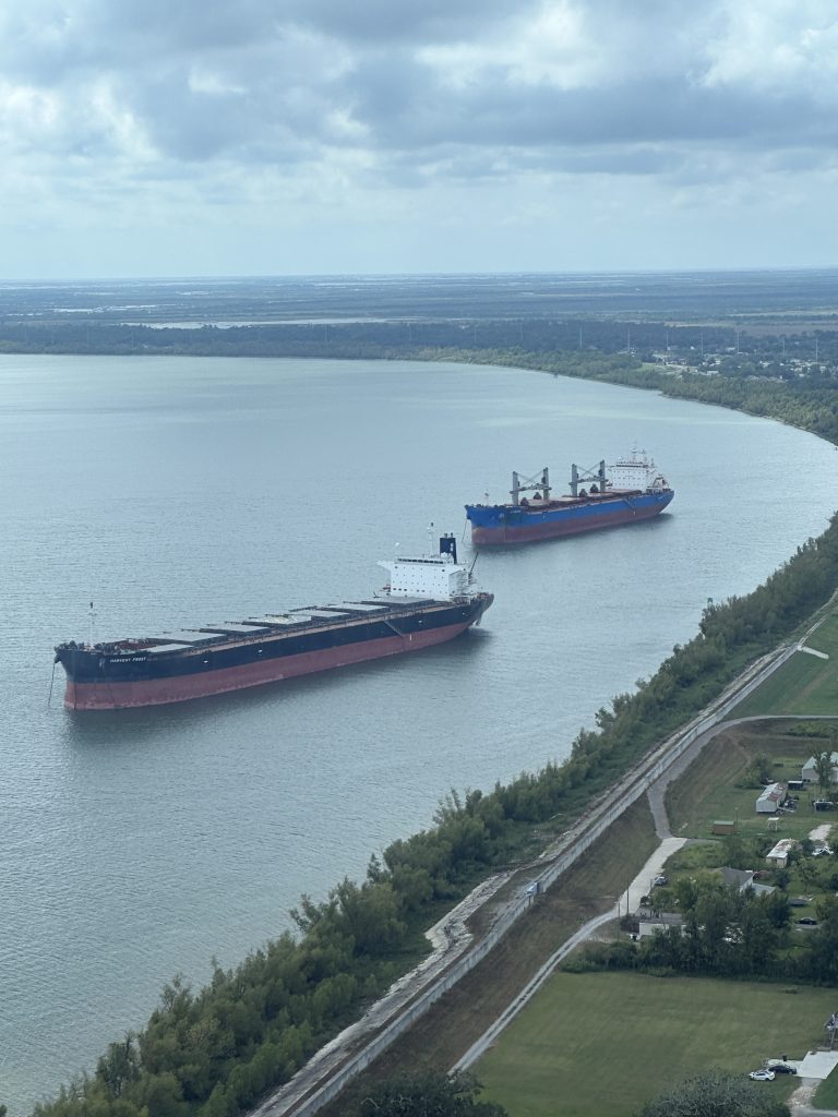 Aerial view of two large bulk carrier ships navigating a wide river channel under a cloudy sky.